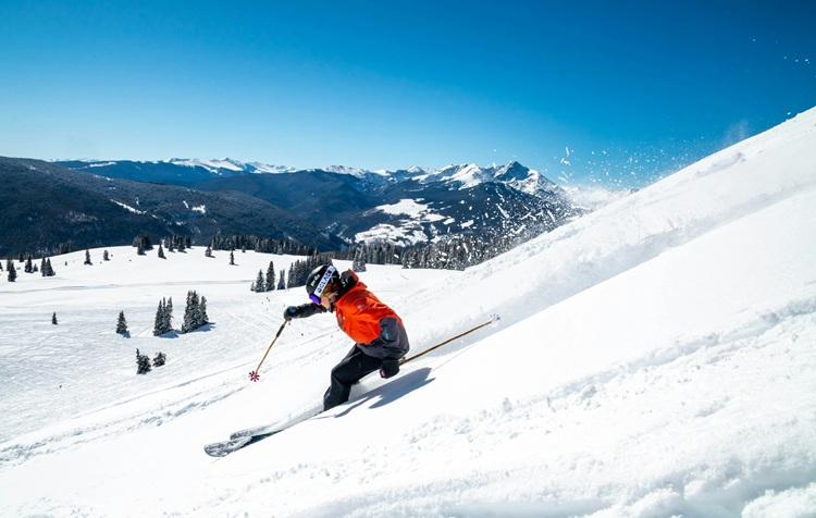 personne en veste orange descend une piste à ski