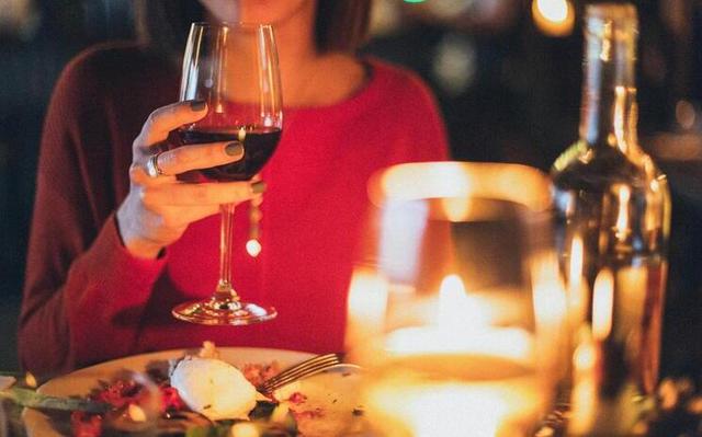 Femme qui tient un verre de vin rouge dans la main dans un restaurant devant une assiette