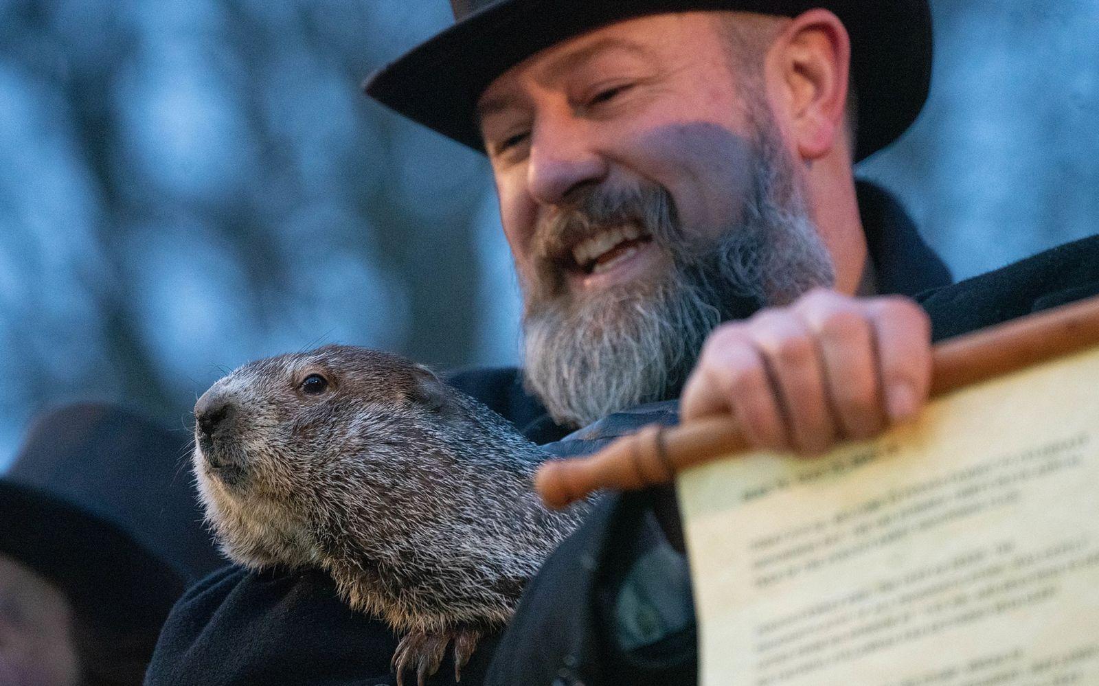 Un homme tient dans ses bras une marmotte et un document.