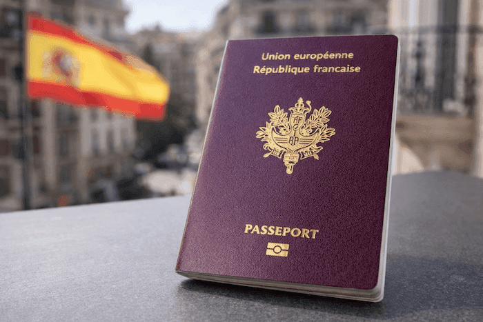 Passeport français posé au premier plan avec un drapeau espagnol flou en arrière-plan, symbolisant les Français vivant en Espagne.