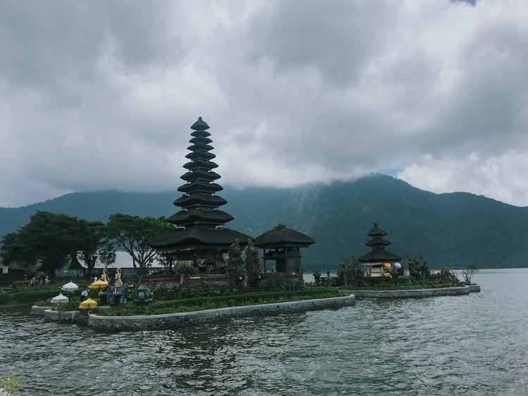 vue d'un temple à bali bordé par un lac avec montagne en arrière plan sous ciel couvert_0