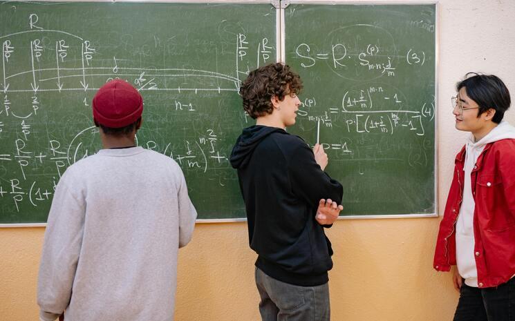 trois étudiants qui tentent de résoudre une équation de mathématiques face à un tableau