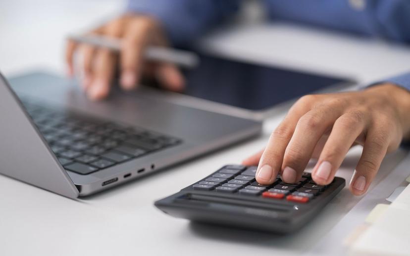 Des mains sur un ordinateur et une calculatrice.