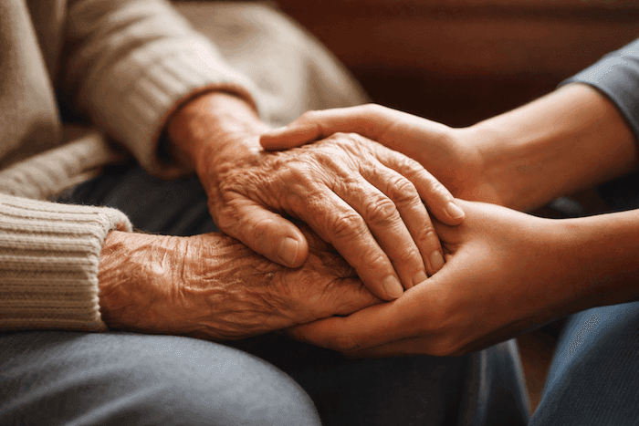 Une personne adulte tient délicatement les mains ridées d’un parent âgé, dans un geste tendre qui évoque le temps qui passe, le lien familial et l’amour entre générations.