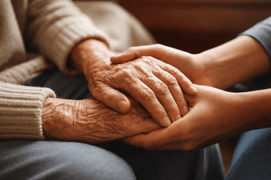 Une personne adulte tient délicatement les mains ridées d’un parent âgé, dans un geste tendre qui évoque le temps qui passe, le lien familial et l’amour entre générations.