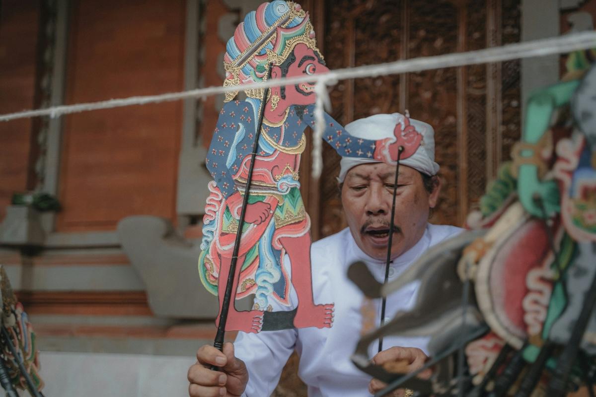 un homme balinais habillé en blanc qui tient une marionette traditionnelle