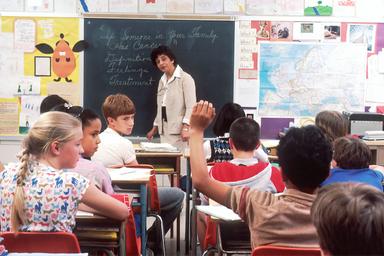 une salle de classe avec des enfants et une institutrice au tableau