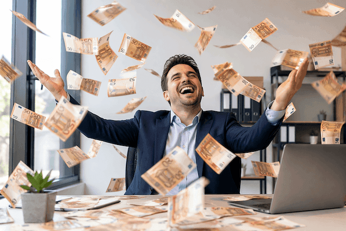 Homme en costume assis à un bureau, lançant des billets de 50 euros en l’air avec un large sourire dans un bureau lumineux, scène symbolisant des salaires élevés et une réussite financière.