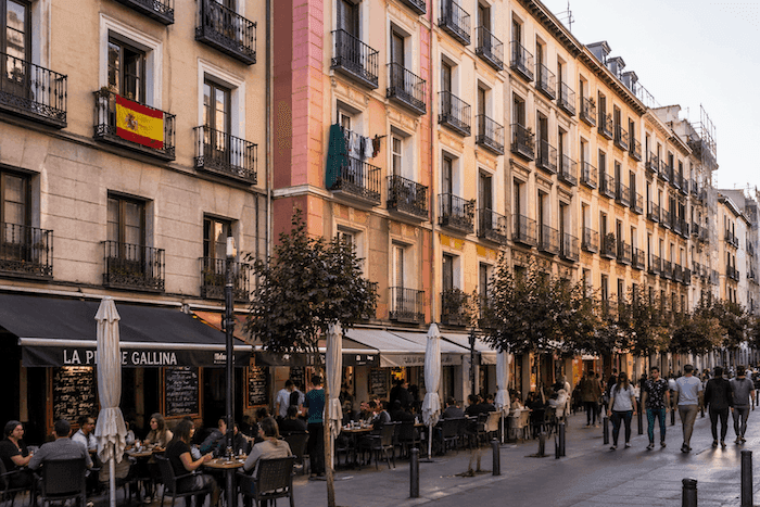 Rue animée bordée d’immeubles à balcons avec terrasses de cafés, illustrant la vie en appartement et la sociabilité urbaine en Espagne.