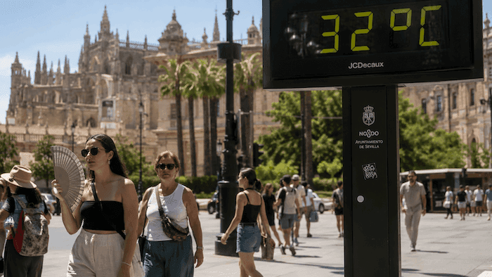 Des passants marchent sous un soleil écrasant à Séville, devant un thermomètre urbain affichant 32 °C en plein mois d’avril, illustrant la chaleur exceptionnelle qui frappe l’Espagne.