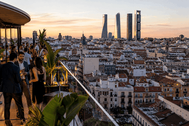 Vue panoramique d’un rooftop de luxe à Madrid au coucher du soleil, avec plusieurs personnes élégamment habillées face à la skyline de la capitale espagnole et aux tours modernes en arrière-plan, illustrant l’essor des grandes fortunes en Espagne.
