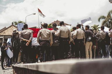un regroupement de policiers en uniforme de dos à bali, avec le drapeau indonésien en arrière plan