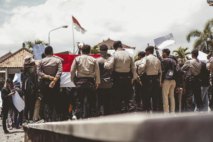 un regroupement de policiers en uniforme de dos à bali, avec le drapeau indonésien en arrière plan