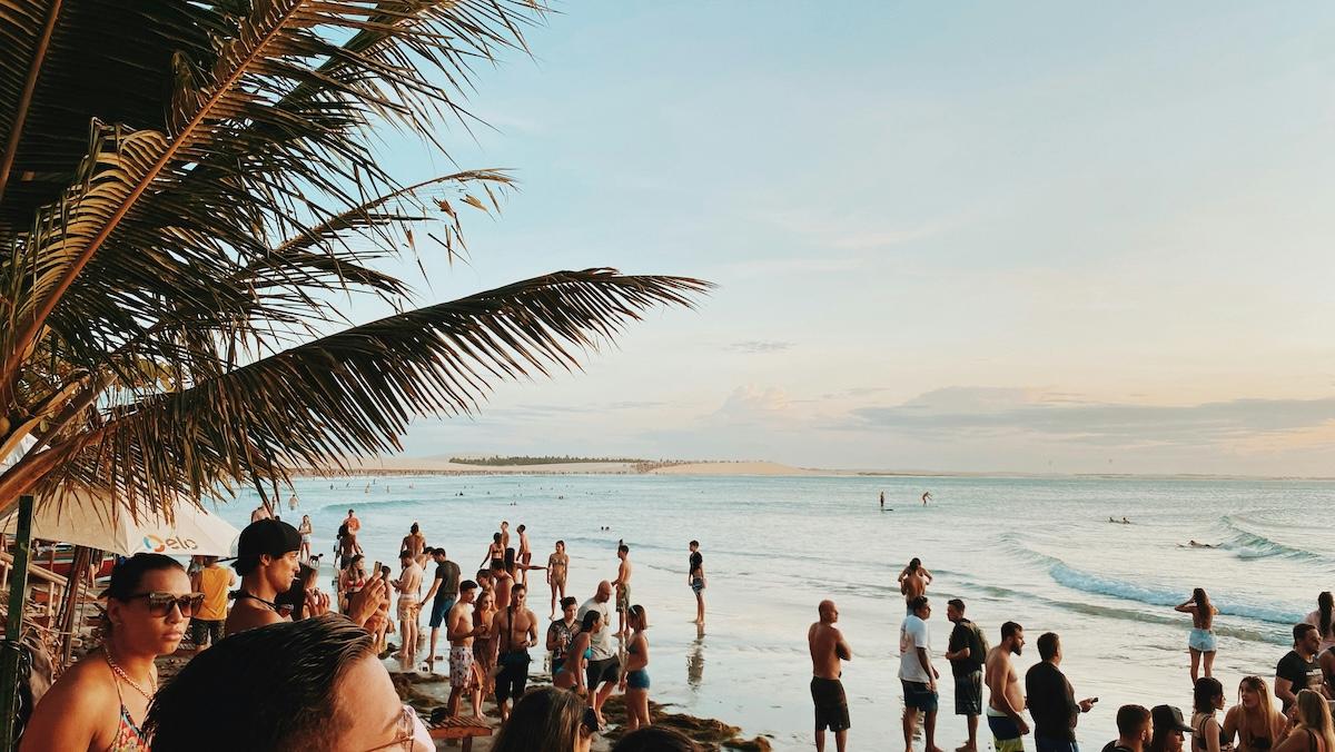 une plage avec une foule de gens et des palmes de cocotiers au premier plan