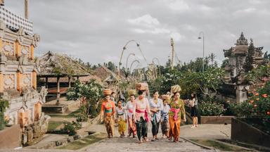 des femmes dans un village de bali avec des sarong colorés qui marchent de face avec des panieres sur la tête