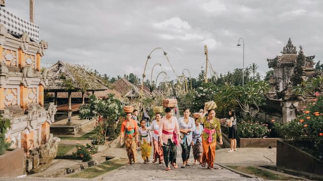 des femmes dans un village de bali avec des sarong colorés qui marchent de face avec des panieres sur la tête