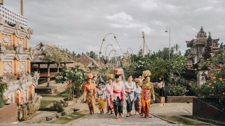 des femmes dans un village de bali avec des sarong colorés qui marchent de face avec des panieres sur la tête