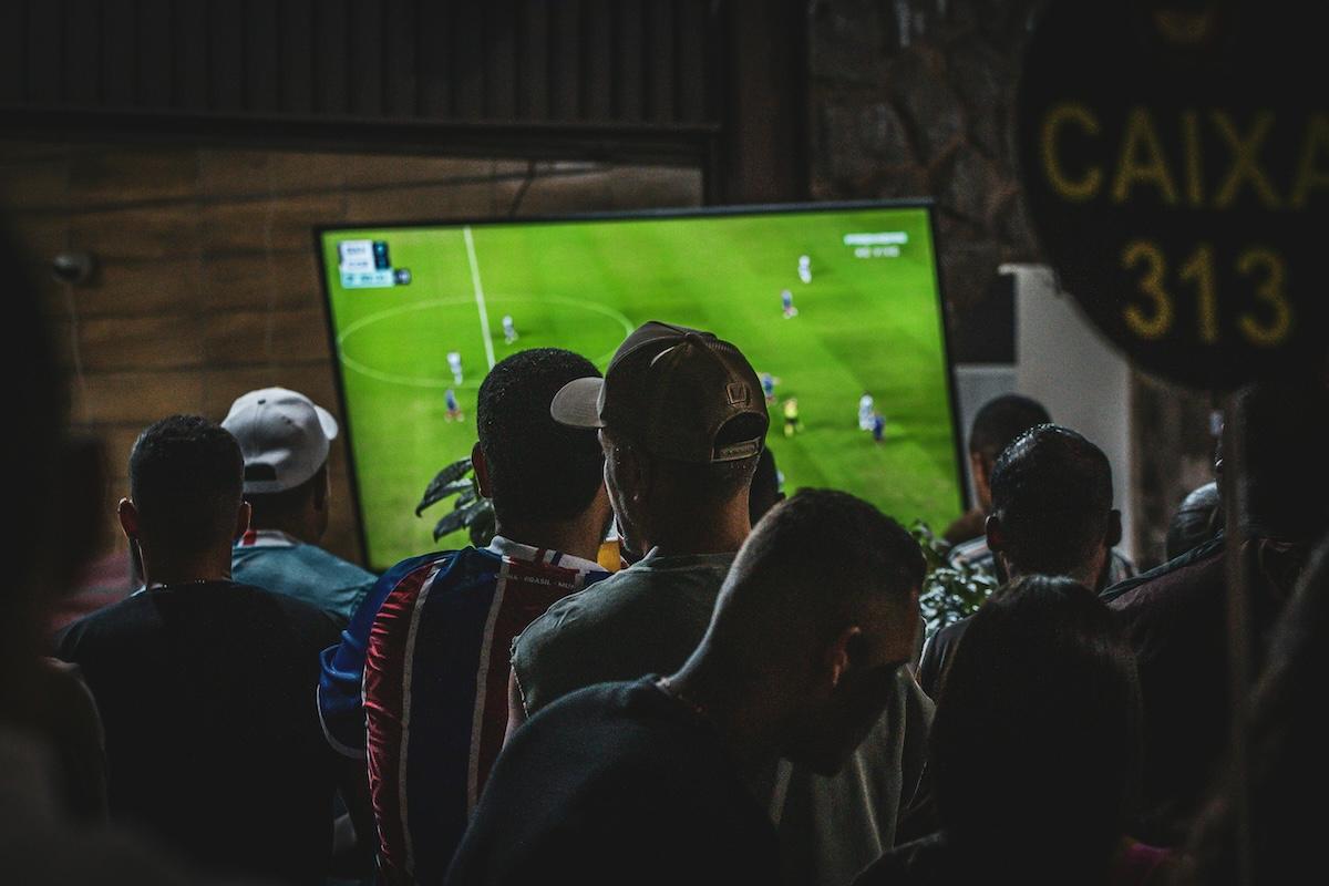 des hommes qui regardent un match de foot sur un grand écran