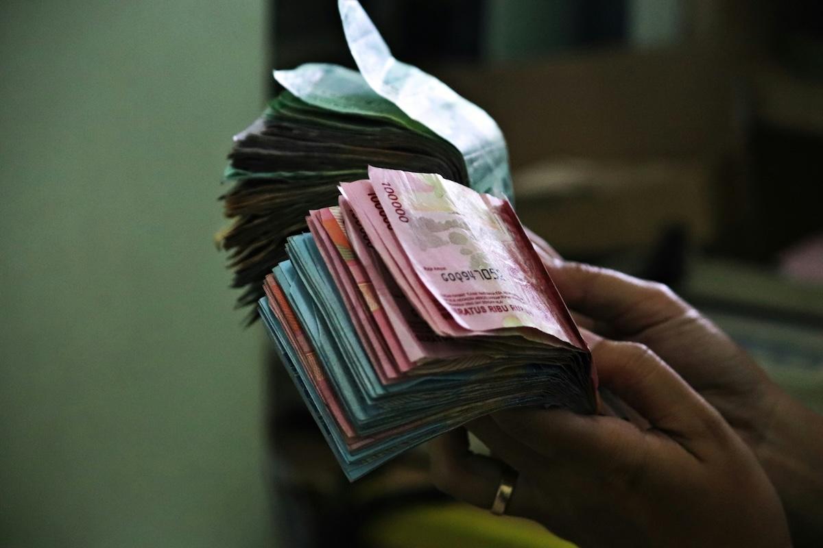 des mains qui tiennent des liasses de billets de roupie indonesienne