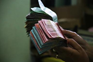 des mains qui tiennent des liasses de billets de roupie indonesienne