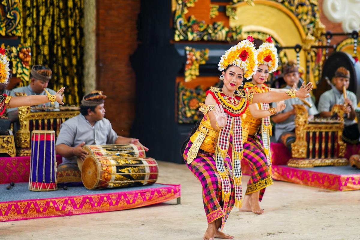 deux femmes balinaises en costume traditionnel jaune et sarong qui dansent avec des musiciens derrière