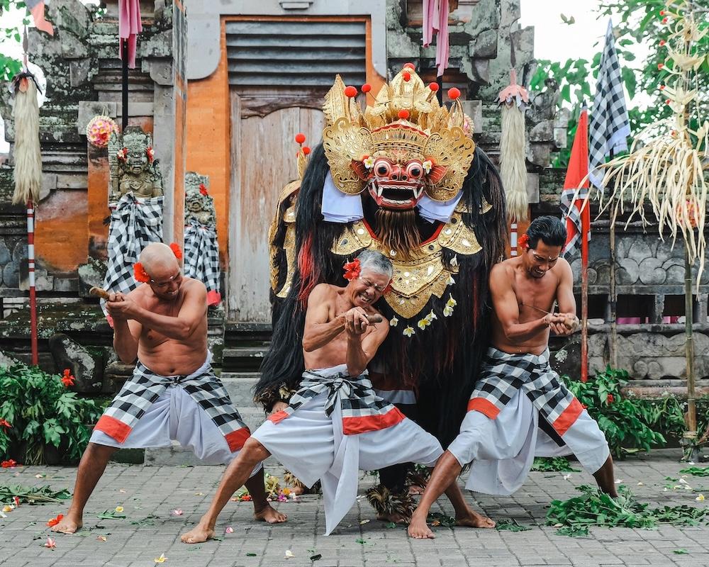 trois hommes en sarong devant un temple et une statue de ogoh ogoh tenant des poignards