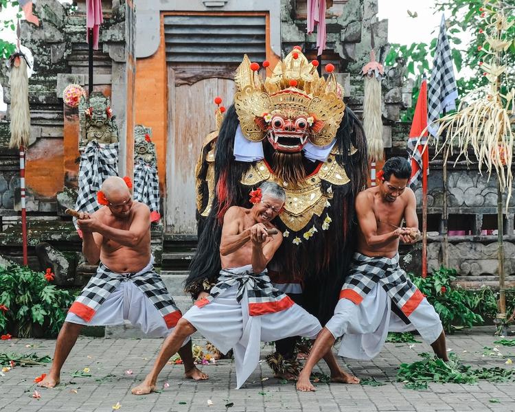 trois hommes en sarong devant un temple et une statue de ogoh ogoh tenant des poignards