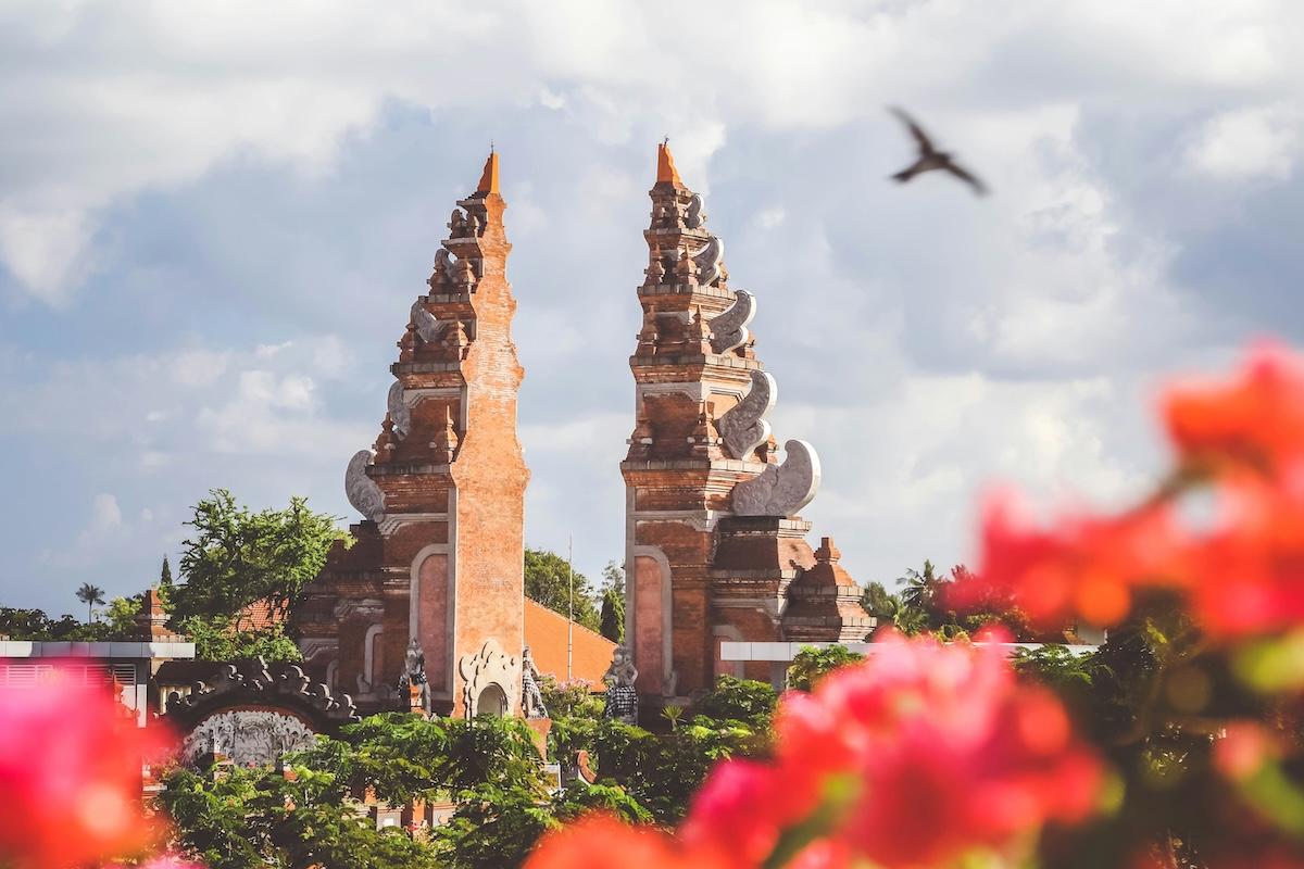 un temple à bali avec des fleurs rouges au premier plan et un oiseau en vol
