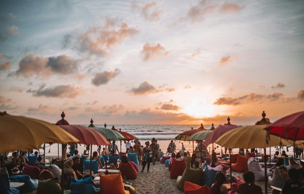 une plage au coucher du soleil bondée de monde et de parasols de différentes couleurs