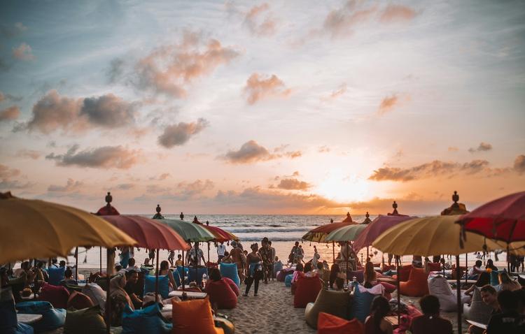 une plage au coucher du soleil bondée de monde et de parasols de différentes couleurs