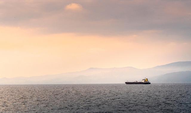 Vue du détroit d'Hormuz au crépuscule prise depuis la mer, un pétrolier et des terres émergées étant visibles à droite de l'image