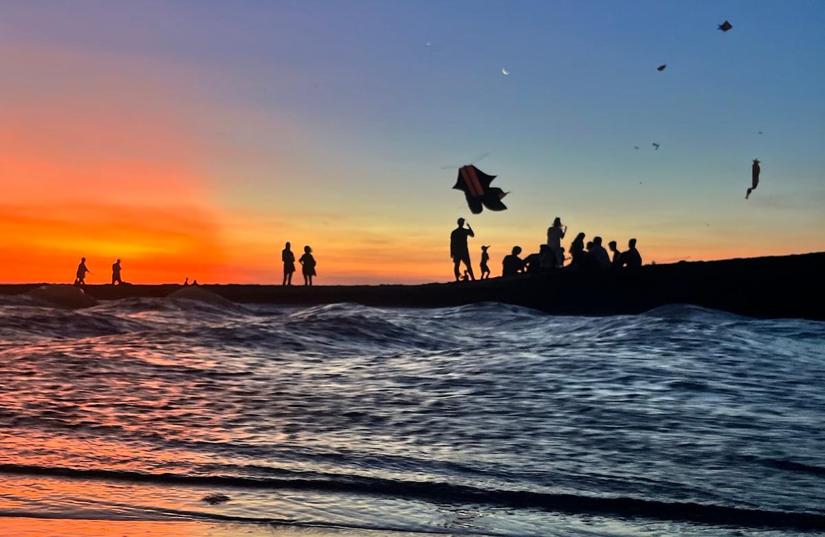 une plage de bali au coucher du soleil avec des cerf volants au loin