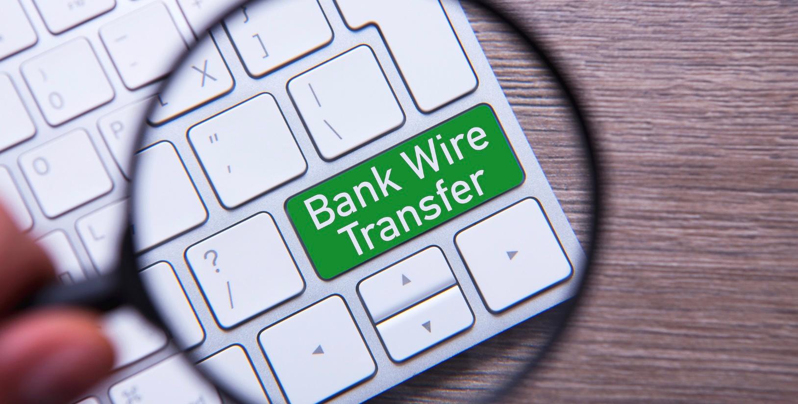 Un loupe sur un clavier avec les mots Bank Wire Transfer