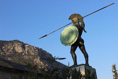 Vue d'une statue représentant un guerrier spartiate, une montagne s'étalant à l'arrière-plan de l'image