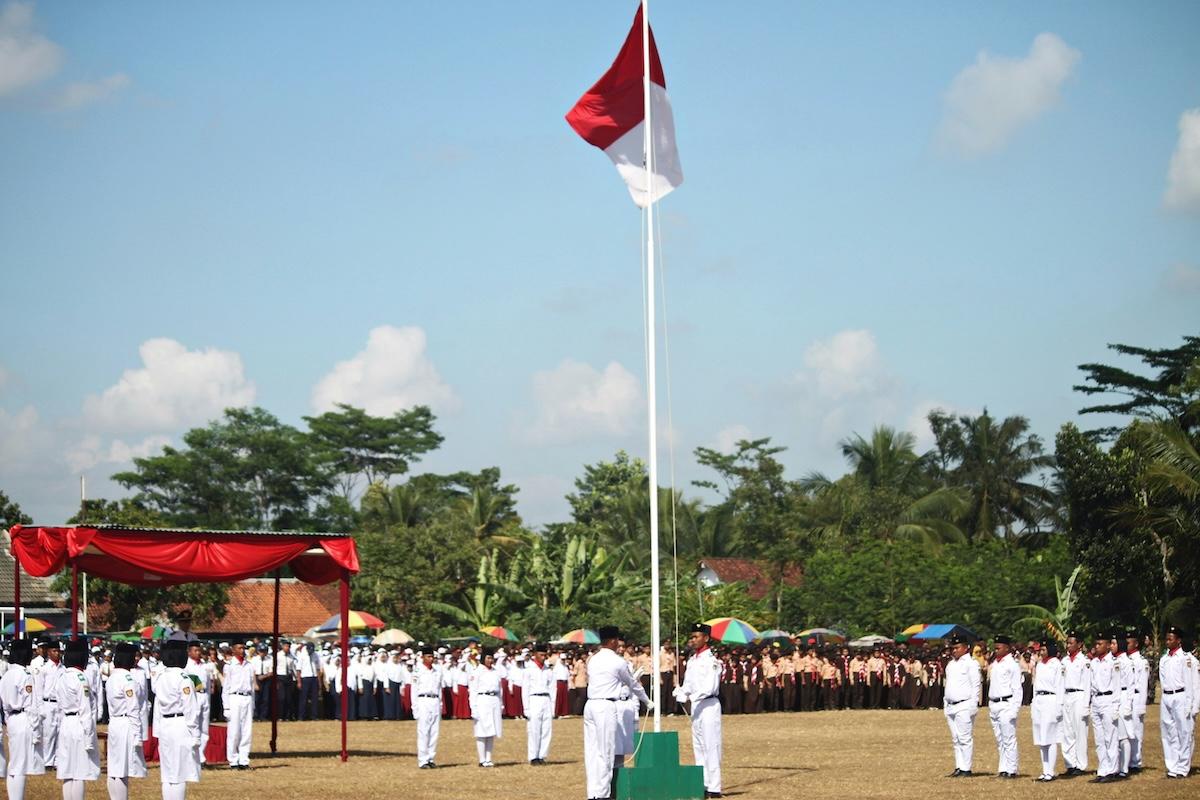une cérémonie de lever de drapeau indonésie avec des hommes en blanc et le drapeau rouge et blanc en haut d'un mat