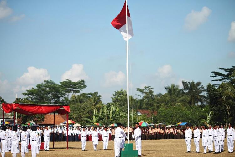 une cérémonie de lever de drapeau indonésie avec des hommes en blanc et le drapeau rouge et blanc en haut d'un mat