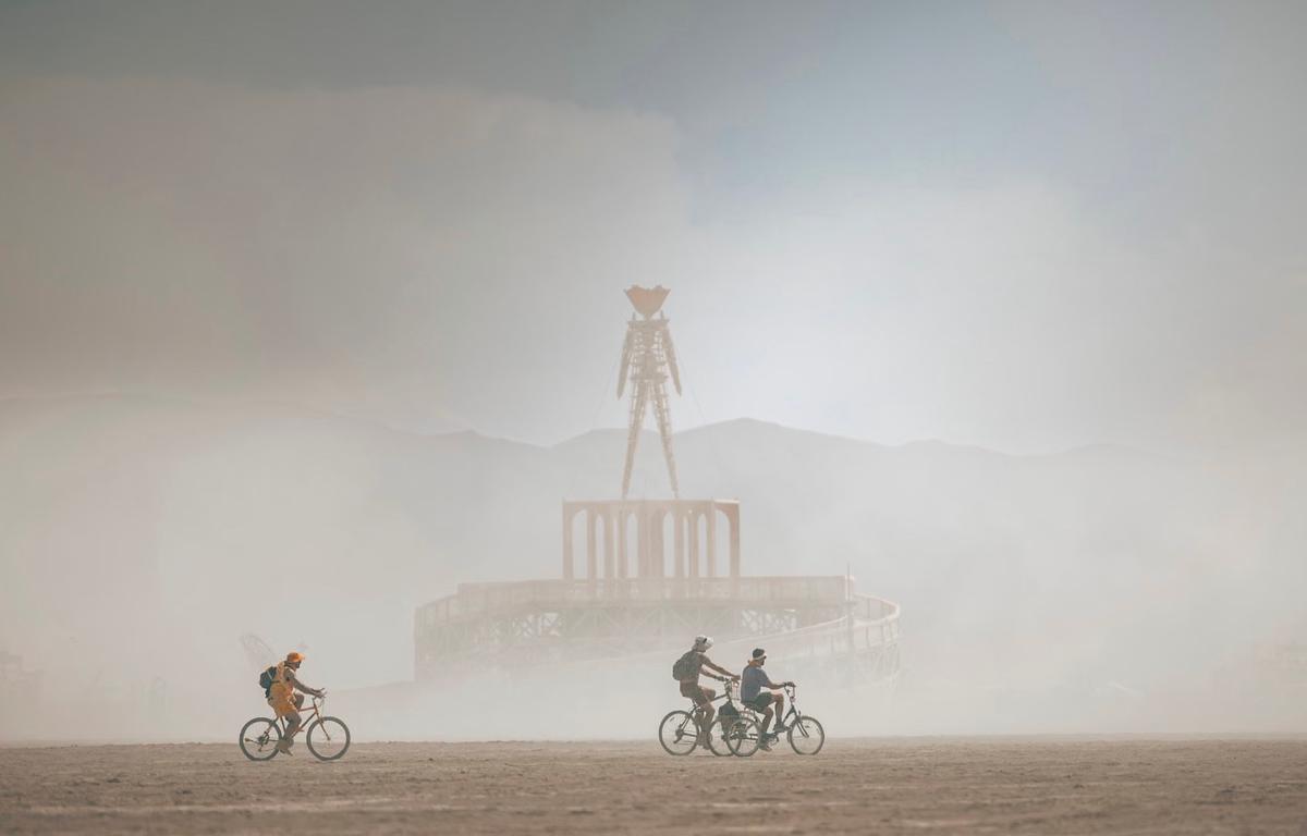 Trois cyclistes roulent dans la poussière au festival Burning Man, près de l'effigie emblématique.