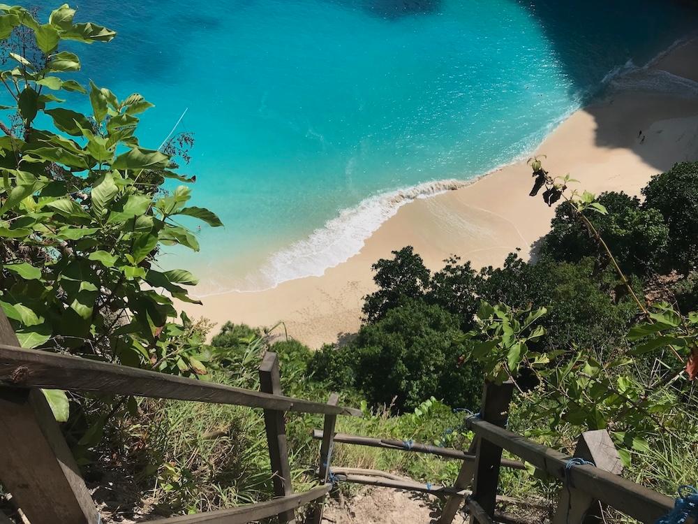 un chemin escarpé sur une falise avec la mer turquoise et la plage en contrebas