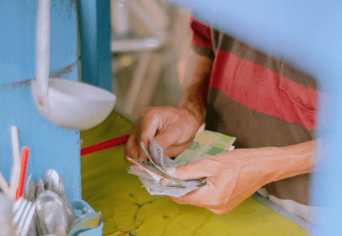 les mains d'un homme qui compte des billets de roupies derrière son stand de nourriture