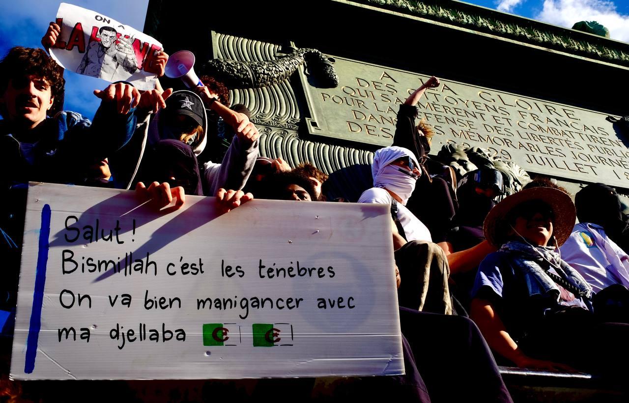 Des manifestants brandissent une pancarte lors d’un rassemblement, devant un monument public, dans un contexte de mobilisation citoyenne.