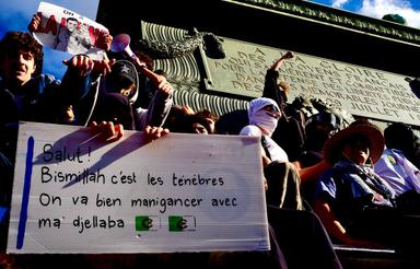 Des manifestants brandissent une pancarte lors d’un rassemblement, devant un monument public, dans un contexte de mobilisation citoyenne.