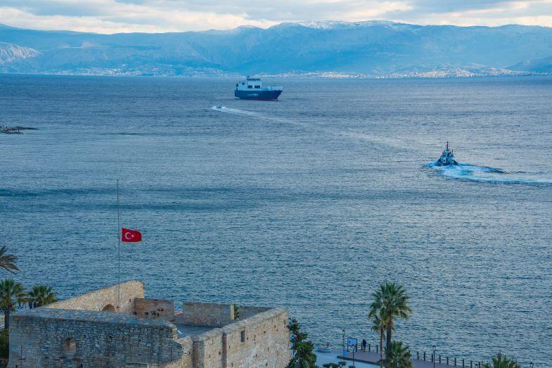Un bateau navigue en mer turque, devant des montagnes. Un drapeau turc est dressé sur un bâtiment.