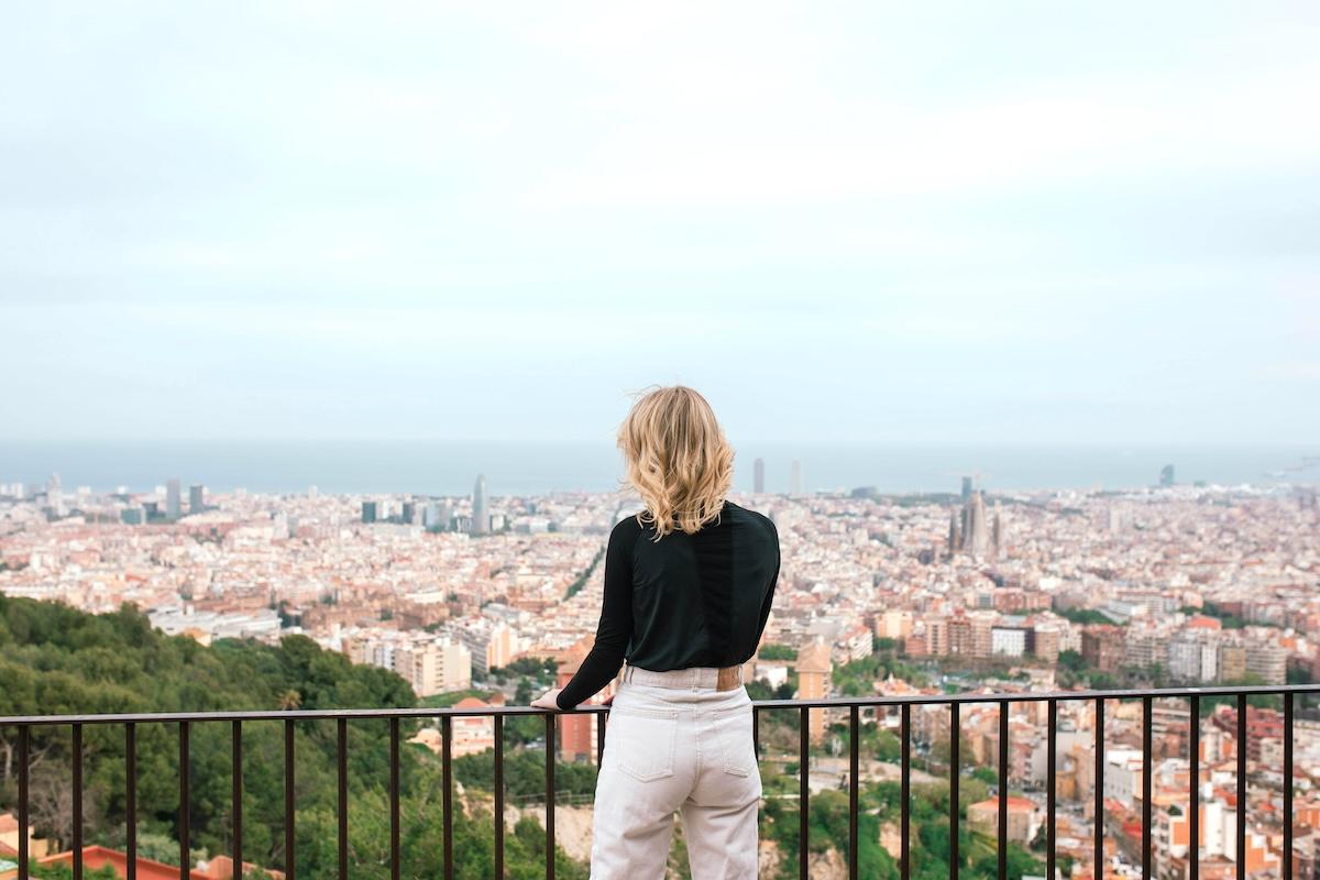 Une femme vue de dos sur un balcon, face au panorama urbain de Barcelone, en Espagne.