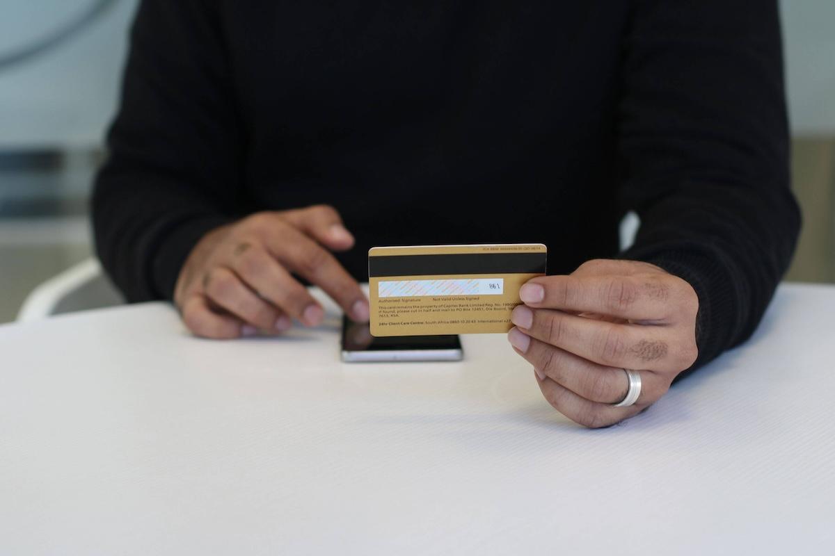 Personne tenant une carte bancaire devant un smartphone, illustration des fraudes bancaires et des remboursements en Espagne.