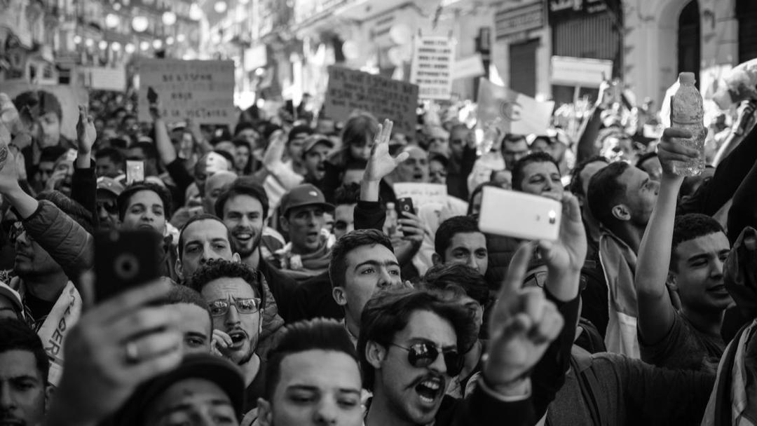 Photographie en noir et blanc montrant une foule dense de manifestants levant leurs téléphones portables pour filmer lors d'un rassemblement politique