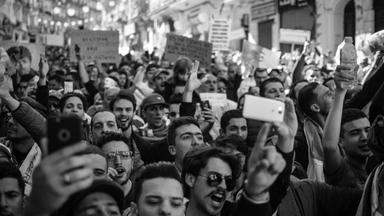 Photographie en noir et blanc montrant une foule dense de manifestants levant leurs téléphones portables pour filmer lors d'un rassemblement politique