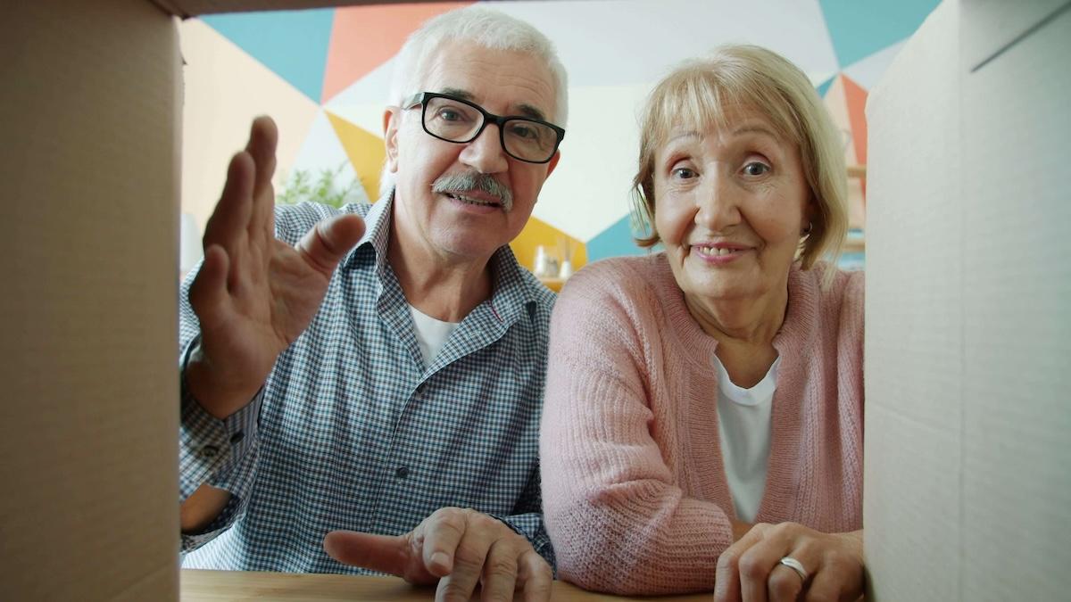 un couple de personnes agees retraitees souriantes regardant dans une boite