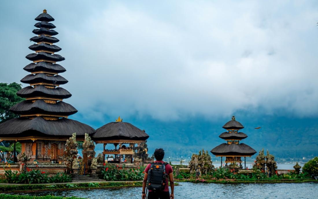 un touriste de dos avec un sac à dos devant un temple sur un lac à bali