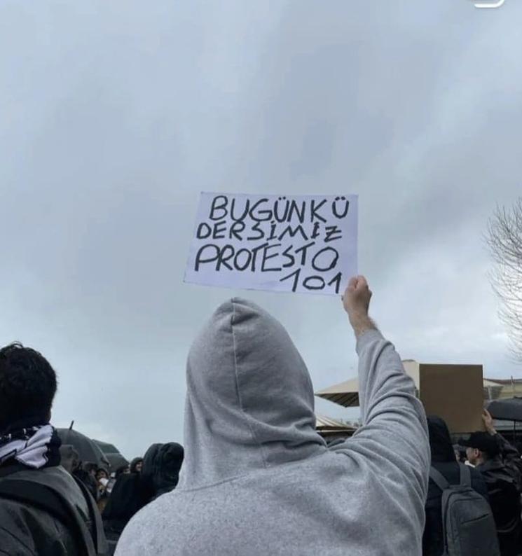 Étudiant tenant une pancarte comparant la manifestation à un cours universitaire