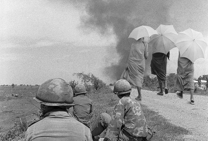 1975_Cambodge_NB_08_28b_3-casques-et-3-bonzes : Mars 1975, Banlieue de Phnom Penh (Cambodge) 3 bonzes marchent vers le front, certains que Bouddha les protègera. Les soldats tentent en vain de les en dissuader. Photo JcTirat.